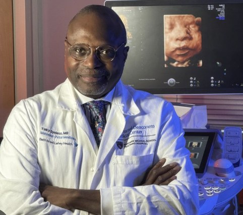 Dr. Yinka Oyelese in a white coat, arms crossed, in an ultrasound room